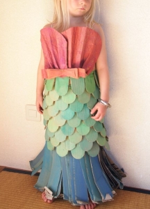 A girl's imagination comes to life as she transforms into a mermaid with a vibrant cardboard mermaid tail. The tail's shimmering colors and wide fin capture the essence of a mythical underwater creature. The girl's joyful expression reflects the magic of DIY costumes and the power of imagination.