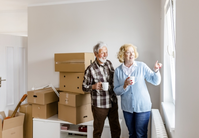 Elderly couple observing moving day activities through a window with anticipation.