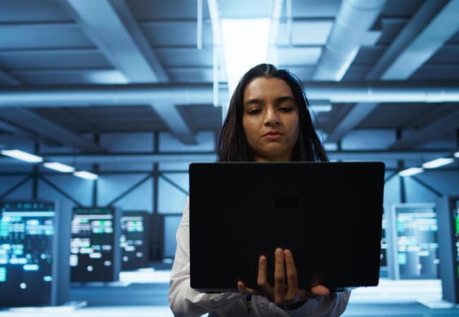 "IT professional assessing systems on a laptop in a high-tech data center, representing strategic planning and analysis for IT relocation services.