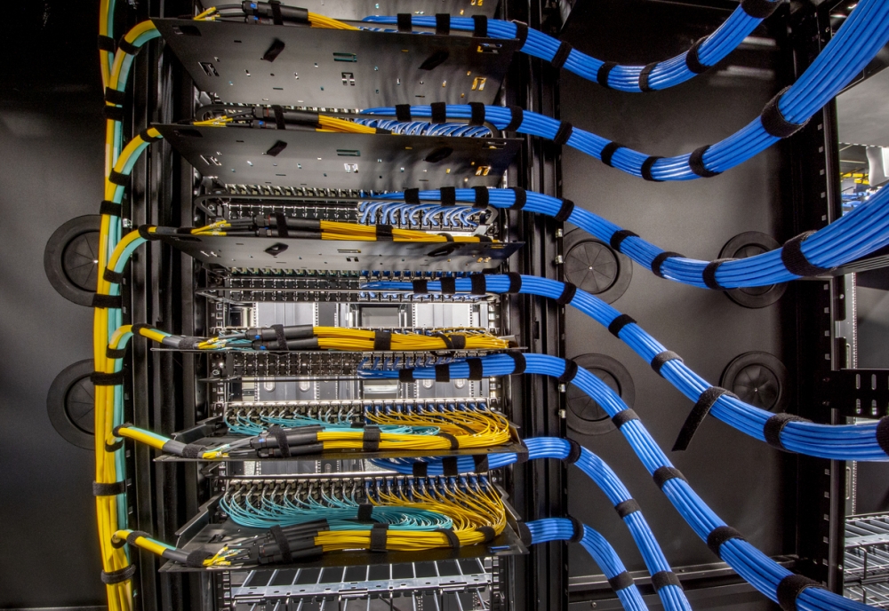 A high-density server rack with precisely bundled blue and yellow network cables, showcasing expert-level cable management during a professional IT infrastructure relocation or data center move.