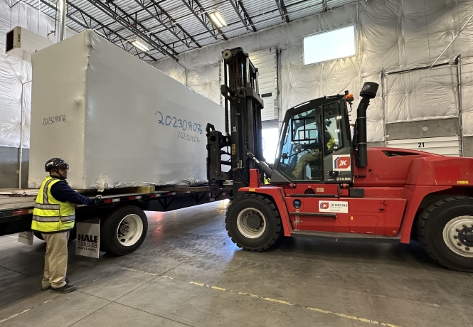 Crane lifting and precisely positioning heavy industrial equipment while workers guide the load in a controlled job site environment.