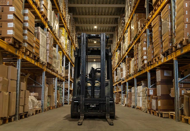 Forklift operator moving palletized equipment inside a large warehouse with organized storage racks.