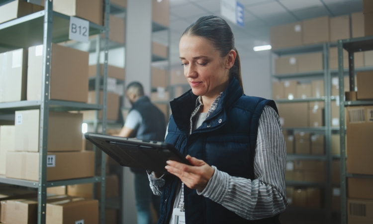 Warehouse worker using a tablet to manage inventory among storage shelves
