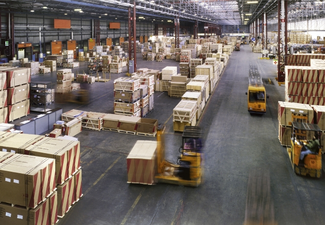 Forklifts transporting packed equipment and crates inside a large industrial warehouse