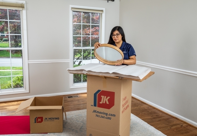 JK Moving crew member carefully packs a round mirror into a branded box during a white glove move